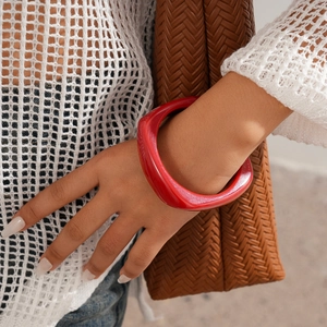 Detail of chunky red resin bangle on wrist with stylish knitted bag and modern accessory