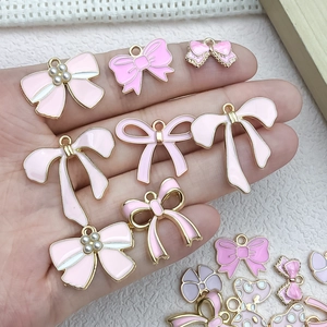 Pink and white enamel bow charms with pearls held in hand for DIY jewelry making