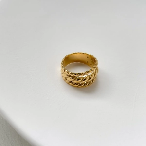 Detailed close-up of a multi-layer gold twisted rope ring on a minimalist white base