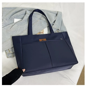 Close-up of navy blue nylon tote bag on denim jacket, showing fabric texture and leather label