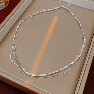 Double-layered silver chain necklace on a beige jewelry tray with warm natural lighting