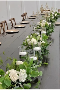 Elegante trouwtafel met drijvende kaarsen in glazen vazen en witte rozen decoratie