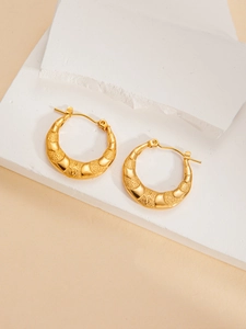 Close-up of golden crescent hoop earrings with star relief on white stone surface