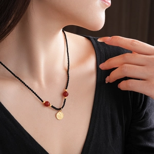 Detail of Fu character gold pendant with red agate beads and black woven cord