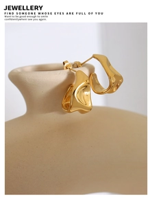 Détail de boucles d'oreilles C dorées irrégulières avec texture martelée sur flacon