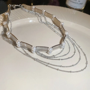Détail macro d'un collier multicouche en perles argentées sur une assiette en céramique