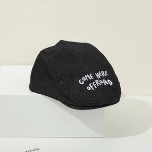 Detailed view of black denim baby beret featuring white 'COME HERE' letter embroidery