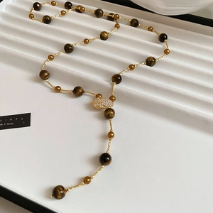 Macro detail of brown tiger eye beads and pavé zircon leaf pendant on vintage necklace