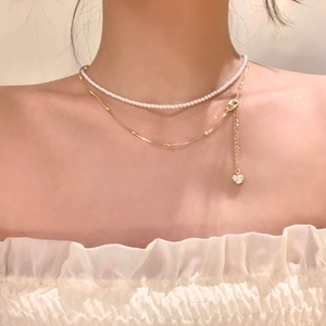 Double-layered necklace with white pearls and a gold heart pendant shown on model