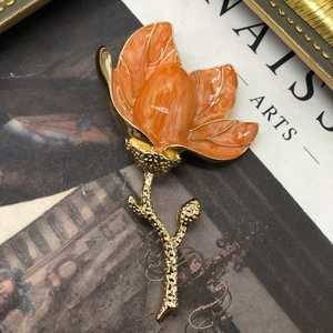 Close-up of elegant orange enamel magnolia brooch with detailed golden stem on art book