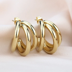 Macro shot of gold-plated triple interlinked hoop earrings on soft pink silk background
