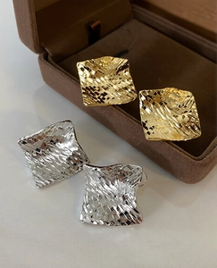 Detail view of square metal stud earrings with woven texture in gold and silver