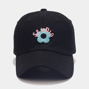 Close-up of STUDIO text and light blue flower embroidery on a black cotton baseball cap