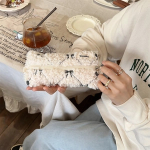 Close-up of cream fuzzy makeup bag with black bow pattern and brand label