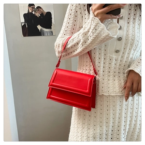 Detail of red leather crossbody bag with flap closure held by model in professional setting