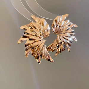 Detail shot of golden pleated metal earrings featuring unique wing-shaped texture design