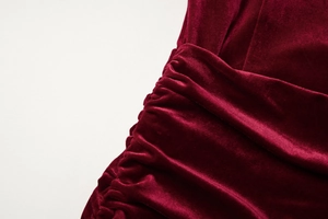 Detailed view of the dark red velvet dress showcasing elegant side ruching and luxury fabric