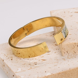 Detailed view of golden wide bangle with colorful enamel pattern on travertine stone