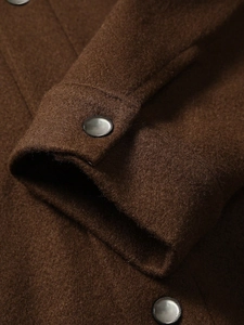 Detailed close-up of dark brown wool jacket cuff with minimalist black polished button