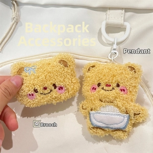 Detail of yellow plush bear brooch and keychain with blue bows on a white canvas bag