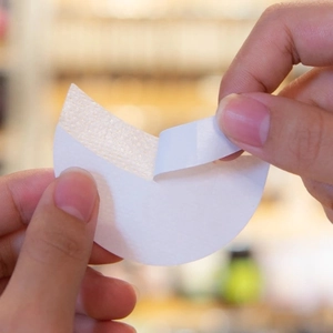 Detail showing the adhesive backing being peeled off a white non-woven eyeshadow sticker
