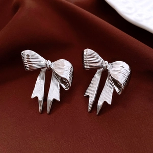 Close-up of silver bow earrings on dark red velvet with metal texture details