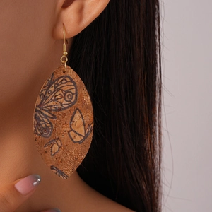 Detail of leaf-shaped cork earrings with butterfly print and gold hooks on model