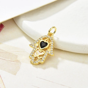 Macro shot of gold Hamsa hand pendant with black heart stone on ceramic tray
