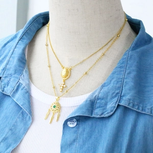 Detail of layered gold necklaces featuring Madonna, cross, and dreamcatcher feather pendant