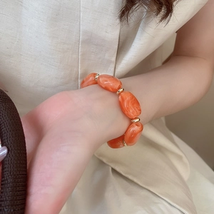 Close-up of orange marble acrylic bracelet with gold beads worn on a model wrist