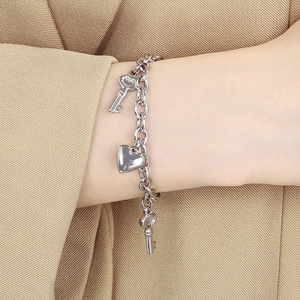 Polished silver stainless steel chain bracelet with heart and key charms worn on a wrist