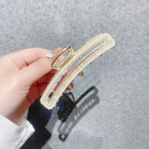 Détail d'une grande pince à cheveux en métal doré ornée de perles blanches et de strass