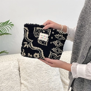 Detail of plush checkerboard makeup bag with logo label held by hand in home setting