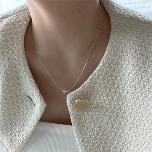 Close-up of minimalist silver fine chain necklace with a single pearl on tweed fabric