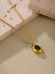 Detailaufnahme einer goldenen Kugelkette mit einem grünen ovalen Edelsteinanhänger im Retro-Stil