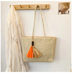 Detail of straw beach tote featuring a paper tassel charm and wooden beads on a hook