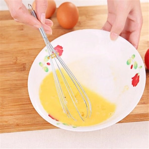 Action shot of stainless steel whisk mixing egg yolks in a white porcelain bowl