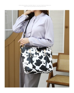 Lifestyle shot of large cow print tote bag with black handles on female model shoulder
