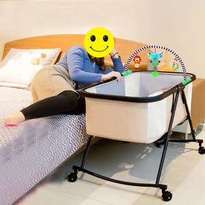 Portable baby crib with black metal frame and hanging activity toys in a home setting