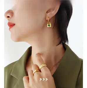 Detail of gold lock earrings with green stones and layered necklaces on a model