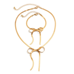 Flat lay of gold bow-shaped snake chain necklace and bracelet jewelry set on white background