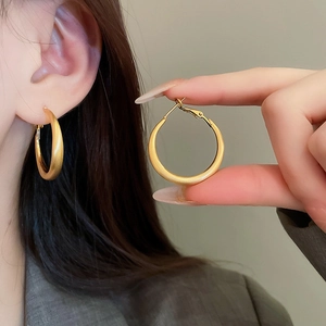 Close-up of matte gold hoop earrings with silver pins worn on model's ear