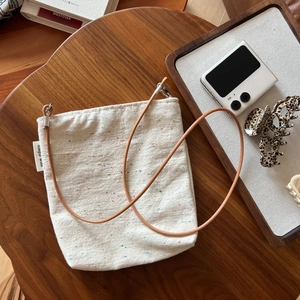 Minimalist canvas crossbody phone bag with leather strap on a vintage wooden table
