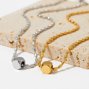 Minimalist gold and silver stainless steel necklace with cube pendant on stone display