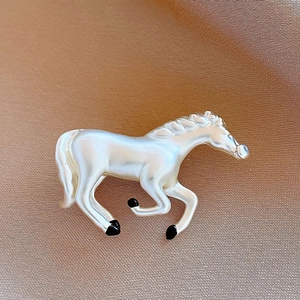 Detailed close-up of a vintage horse brooch with white pearl luster and black accents
