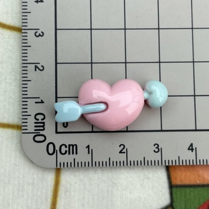 Size measurement of pink heart bow resin charm with arrow showing 3cm width on grid ruler