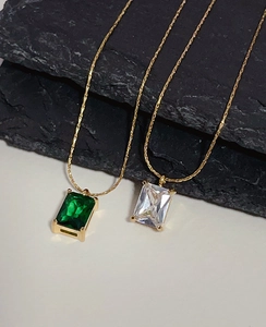 Detail of emerald cut green and white zircon pendants on a golden titanium steel chain
