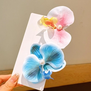 Detail view of pink and blue orchid hair clips with pearl centers on a white card