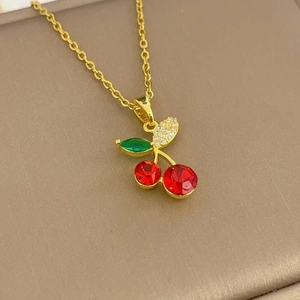 Macro shot of gold cherry pendant necklace with red crystals and green leaves on leather
