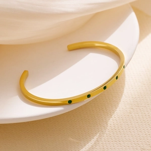 Close-up of gold plated stainless steel cuff bracelet with five inlaid green gemstones